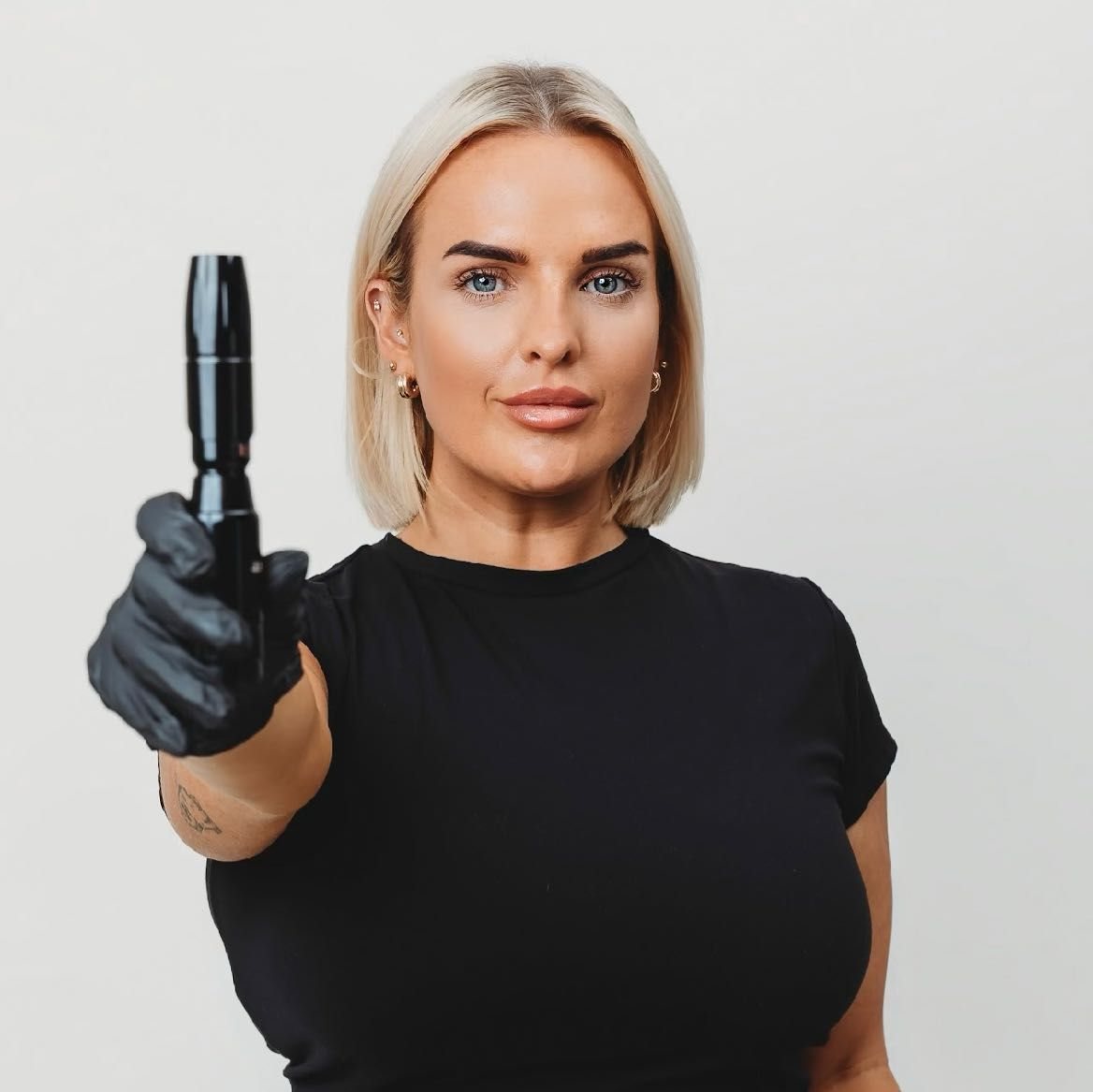 Bethany Webster holding a permanent makeup machine towards the camera