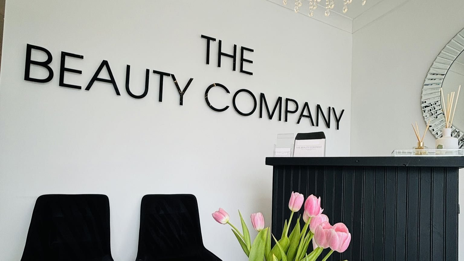 The reception at The Beauty Company: the wall sign, a black desk and pink tulips
