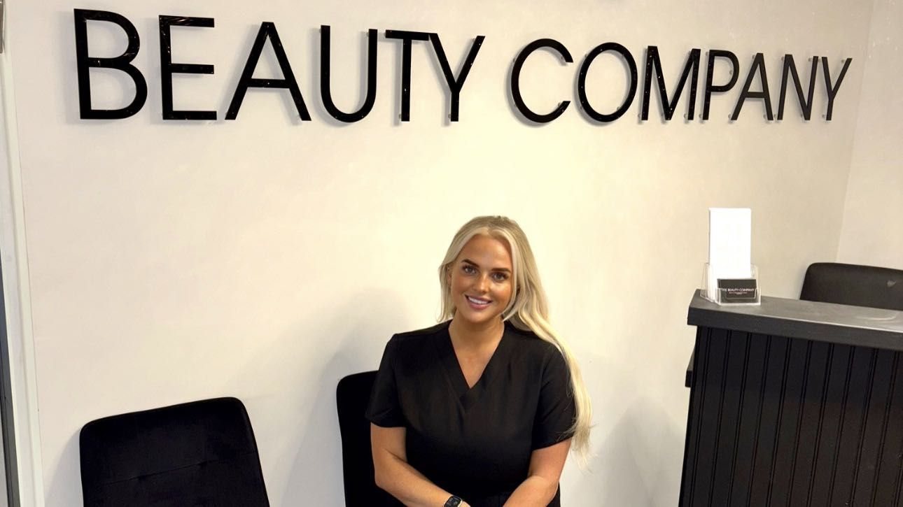 Beth seated in the reception beneath The Beauty Company sign