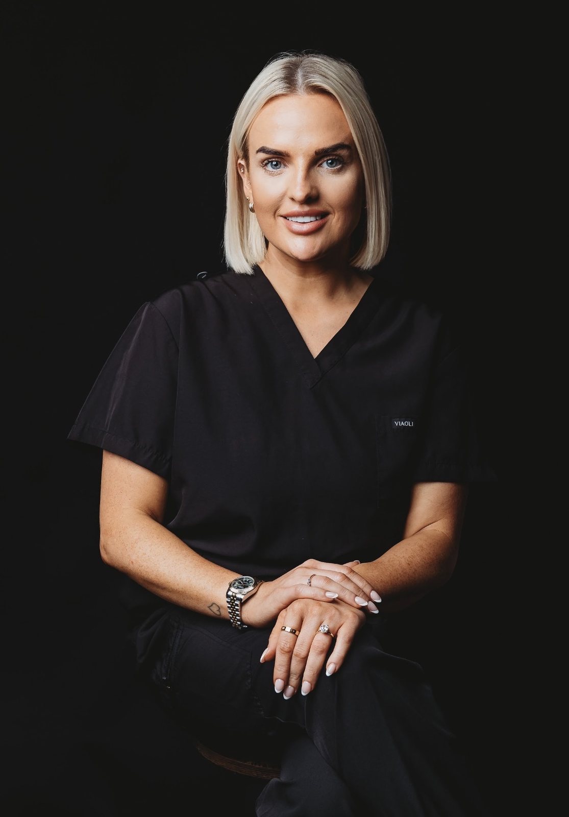 Bethany Webster of The Beauty Company, seated in black scrubs