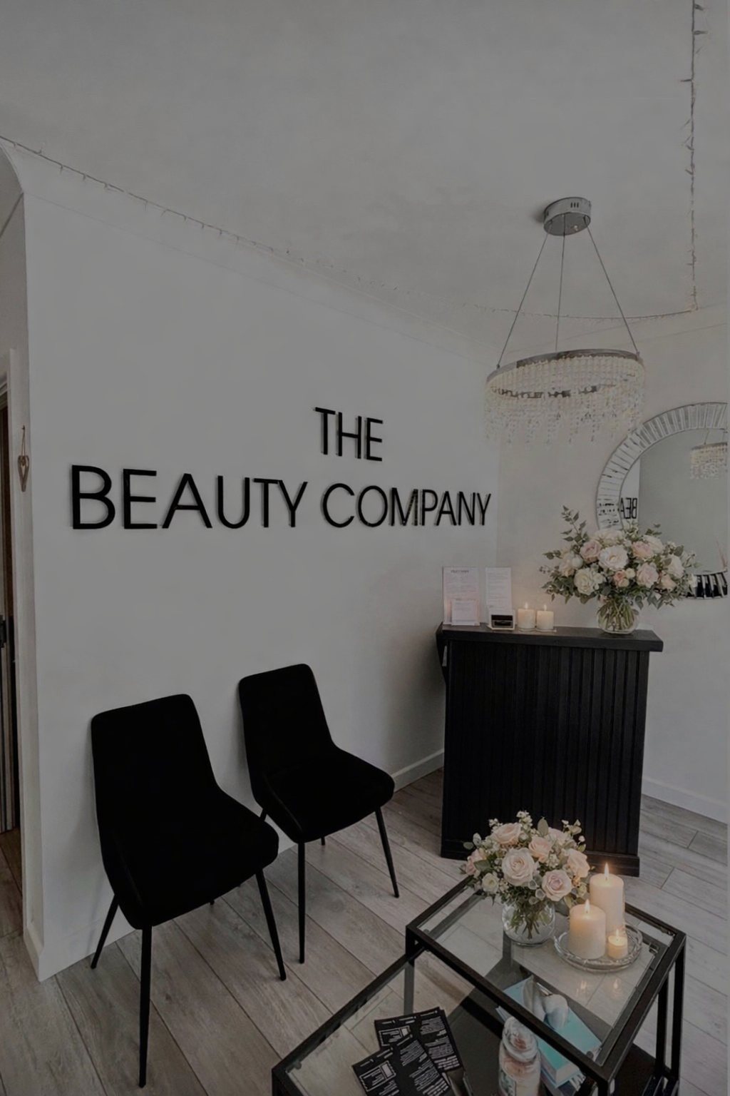The reception at The Beauty Company with its wall sign, black chairs and chandelier